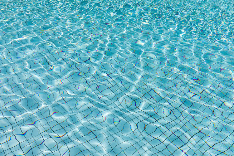 Sun reflection in blue water of swimming pool, shining blue water ripple, aqua texture, pattern