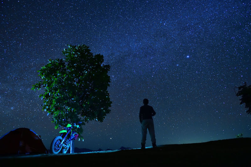 Silhouette man standing by tree against sky at night