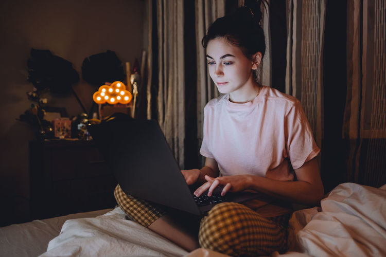 Young woman using phone while sitting on bed at home