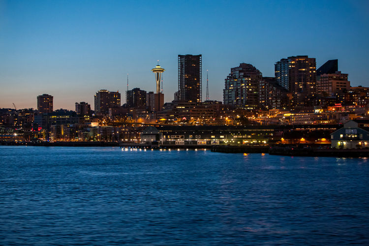 Illuminated buildings by sea against sky at night