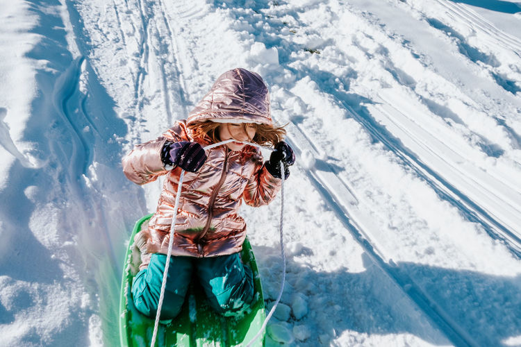 High angle action shot of young girl sledding down a hill in winter