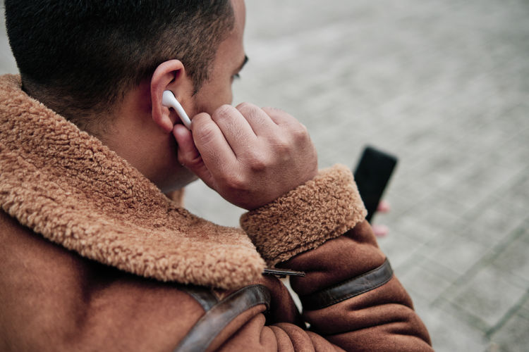 Young man putting on his earphones to listen to music on his phone on the street