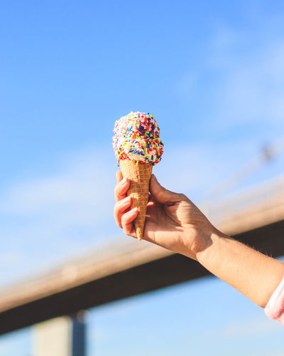 Person holding ice cream cone against sky