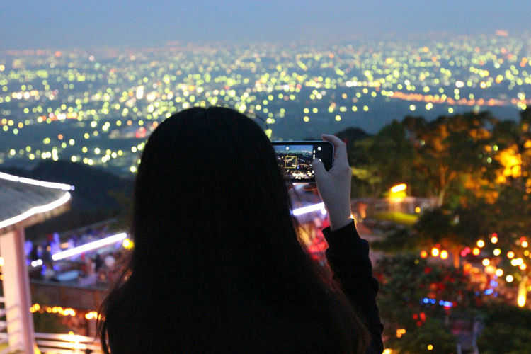 Rear view of woman photographing illuminated cityscape at night
