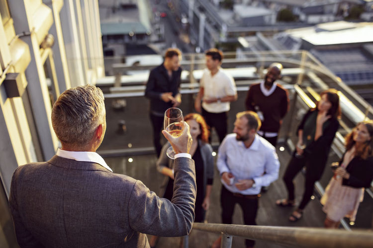 Mature businessman raising toast while giving speech to colleagues in terrace
