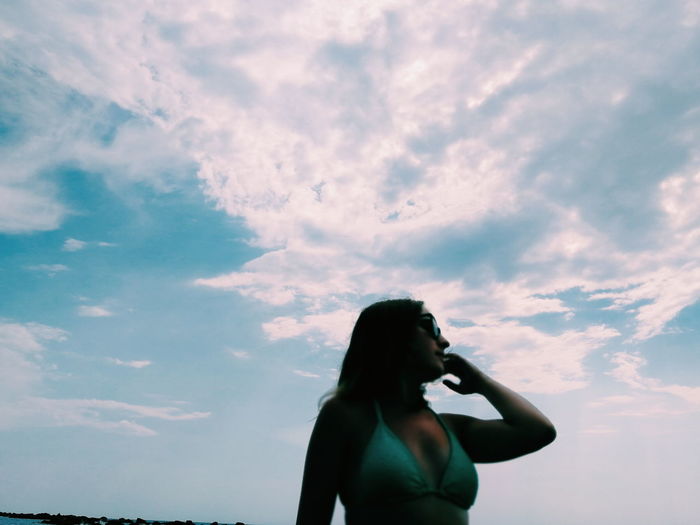 Young woman wearing bikini top standing against sky