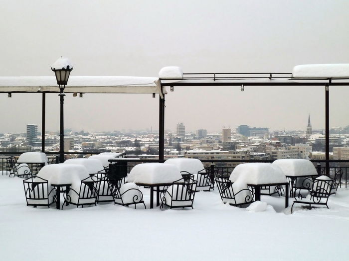 Empty chairs and tables in winter against sky