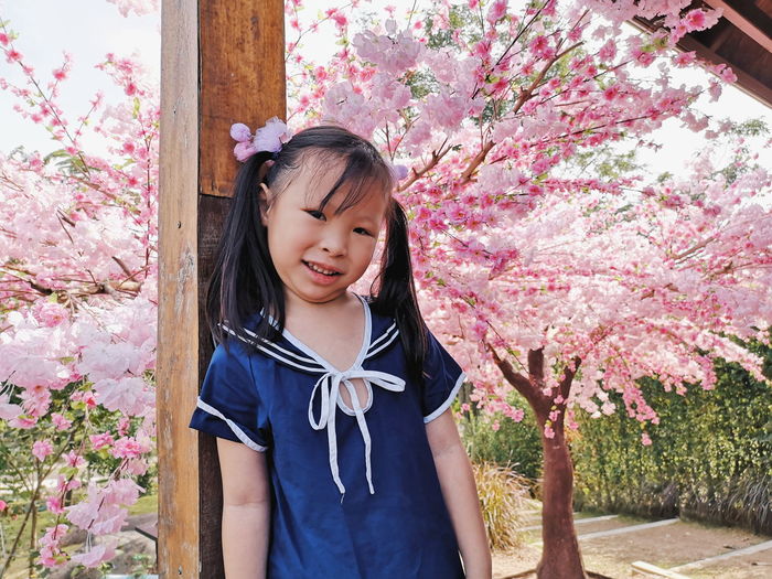 Portrait of girl standing against pink flowers on tree