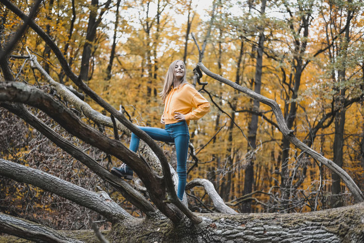 Full length of girl standing on tree trunk in forest