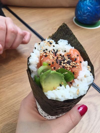 Cropped hand of woman holding sushi roll over table