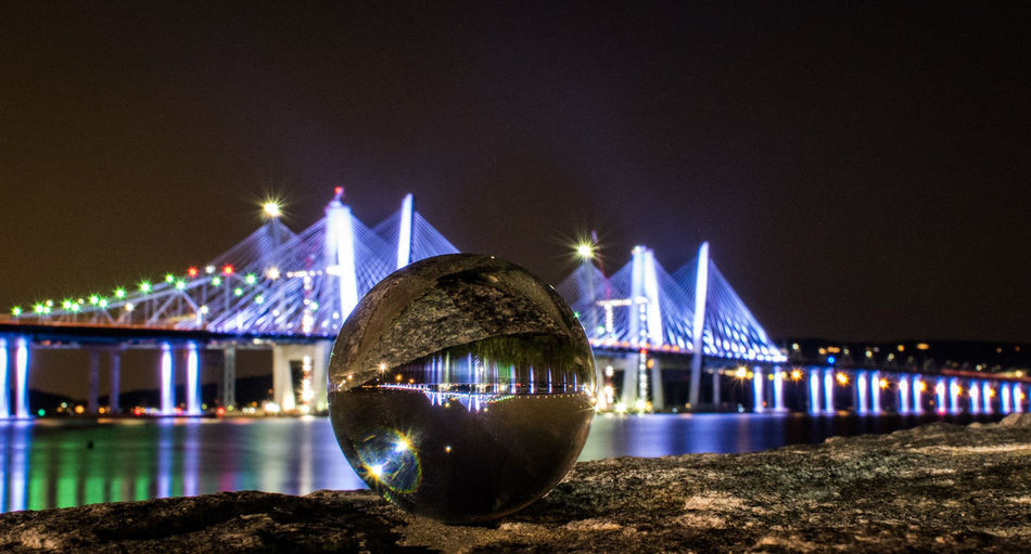 Close-up of crystal ball against illuminated cable-stayed bridge at night