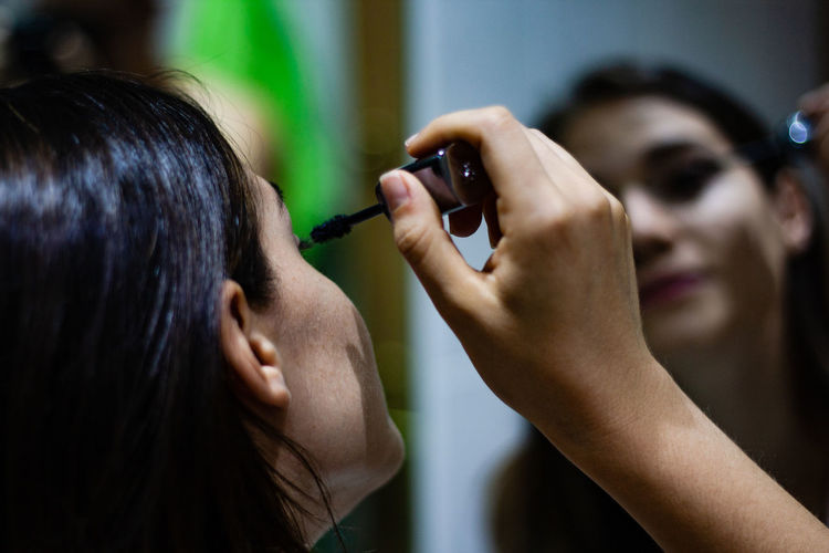 Close-up of woman applying mascara against mirror