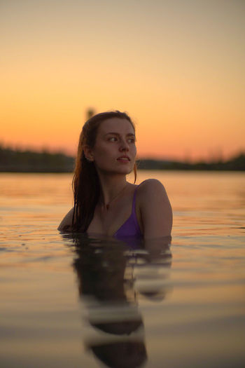 Portrait of young woman swimming in lake during sunset