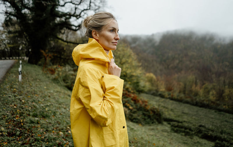 Pretty woman in yellow raincoat walking in rainy weather in the countryside