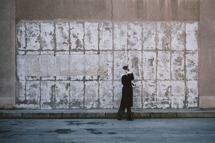 Side view of man using mobile phone against wall