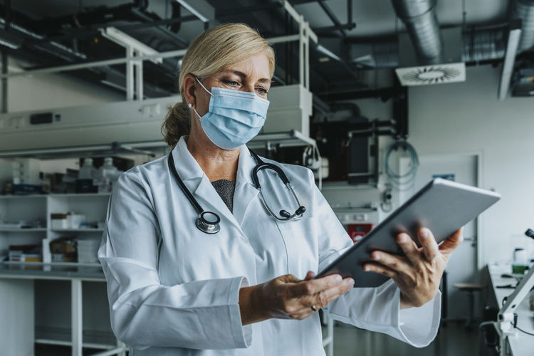 Scientist wearing face mask using digital tablet while standing at laboratory