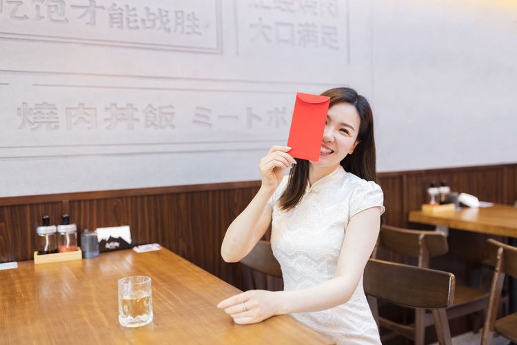 Portrait of smiling woman holding envelop at cafe