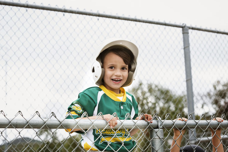 Portrait of cheerful boy in baseball uniform against clear sky