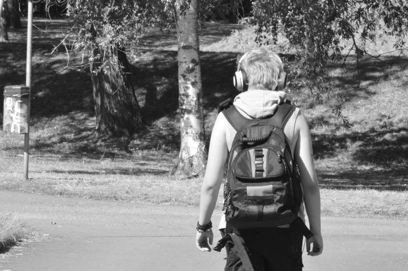 Rear view of backpack man walking on road during sunny day