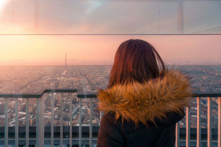 Back view of unrecognizable female tourist standing on viewpoint and admiring cityscape with eiffel tower in paris at sundown