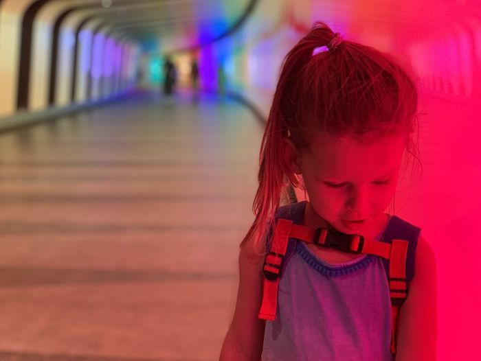 Close-up of girl looking down while standing in illuminated corridor