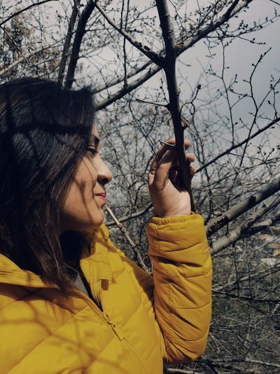 Woman looking away while standing by bare tree