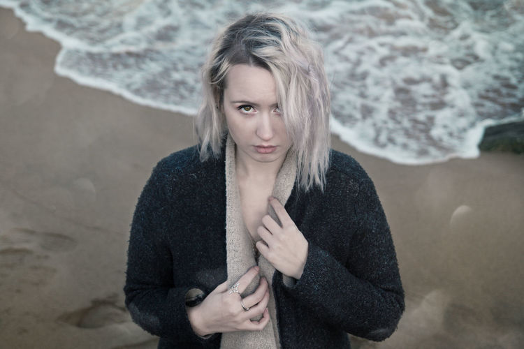 High angle portrait of young woman wearing winter coat while standing on shore