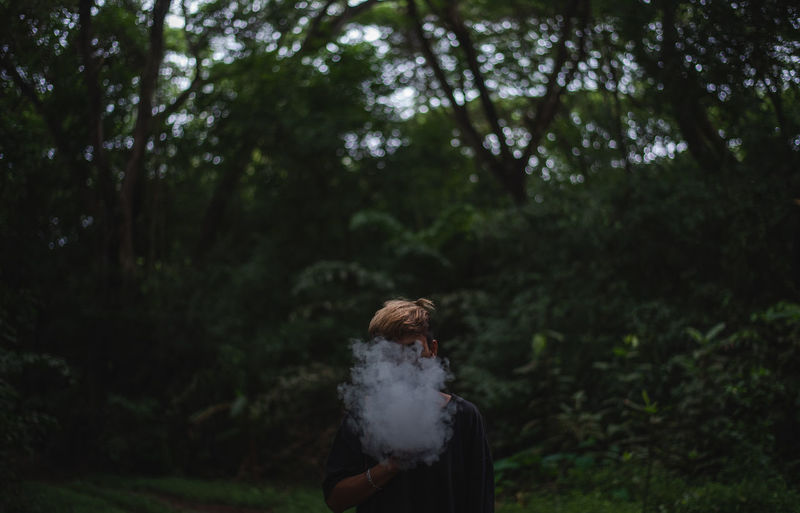 Man with smoke covering face standing against trees