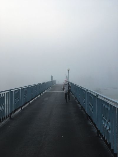 Rear view of man walking on bridge against sky