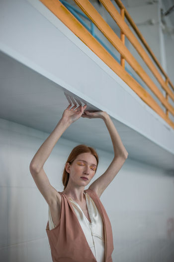 Teenage girl with arms raised and eyes closed standing against wall