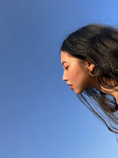 Close-up of young woman looking away against clear blue sky
