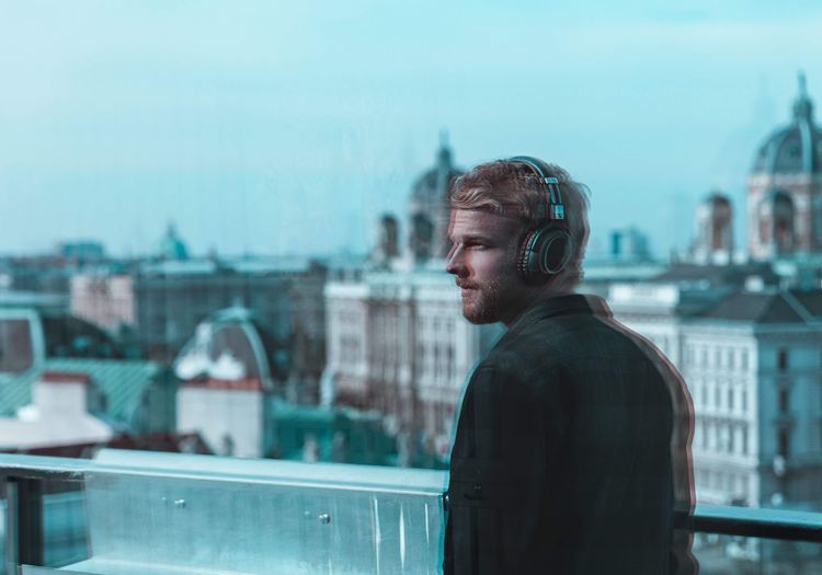 Blurred motion of thoughtful man listening to music through headphones in city