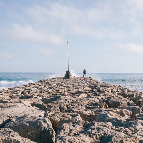 Man fishing at beach against sky