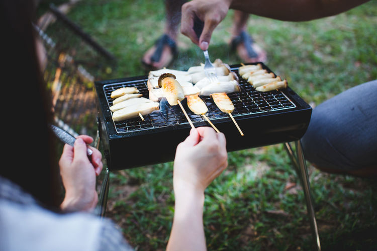 Close-up of people preparing food on barbecue grill in yard