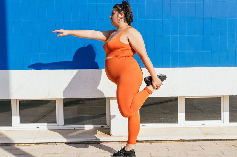 Side view of plump female athlete in sportswear exercising on tiled walkway in sunny town