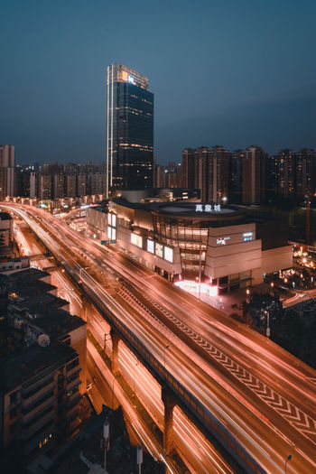 High angle view of light trails on road by buildings against sky