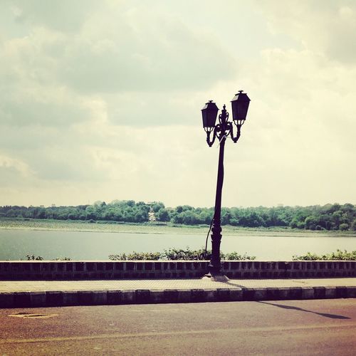 Street lamp by river against cloudy sky