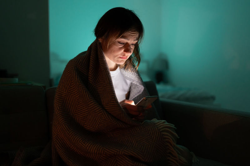 Sleepy woman sitting on couch using smartphone late at night, can not sleep. insomnia, addiction.