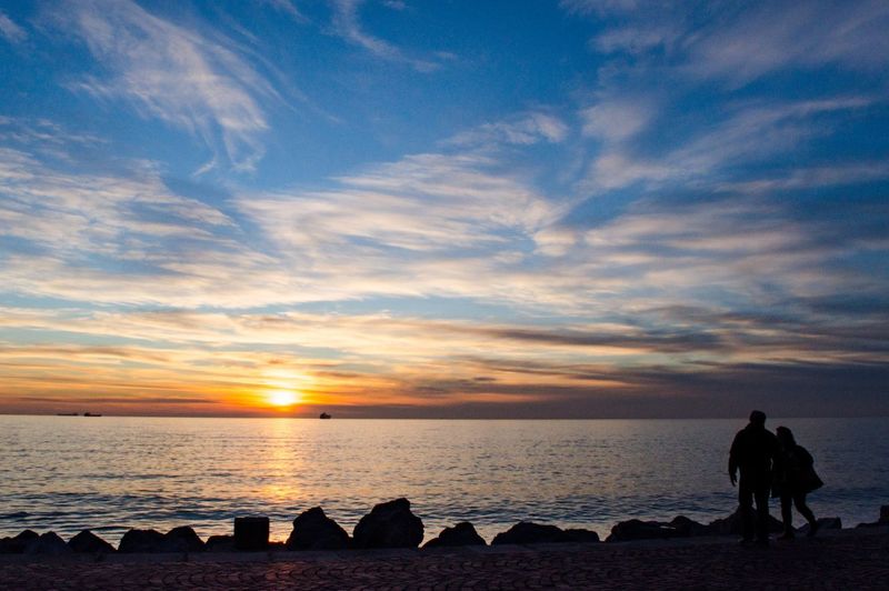 Silhouette people on beach against sky during sunset