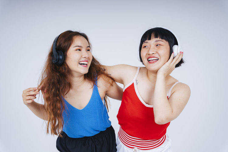 Lesbian couple listening music while dancing against gray background