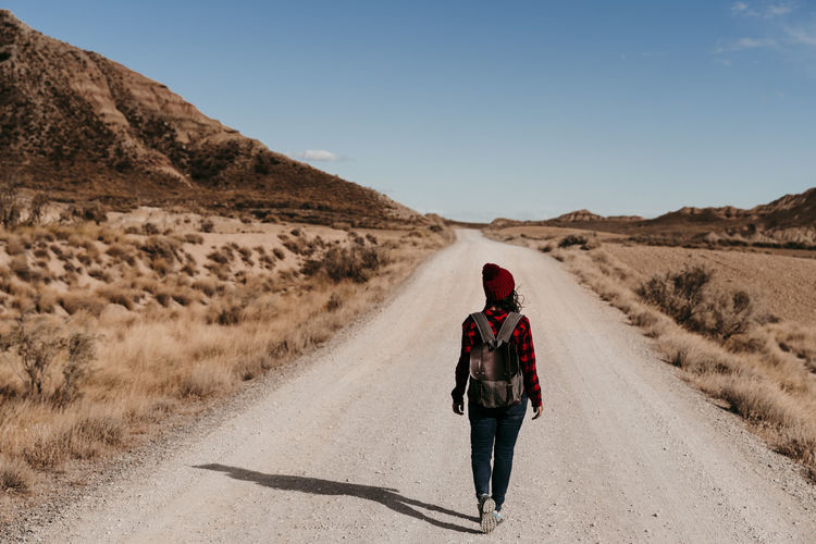 Spain, navarre, female tourist walking along empty dirt road in bardenas reales