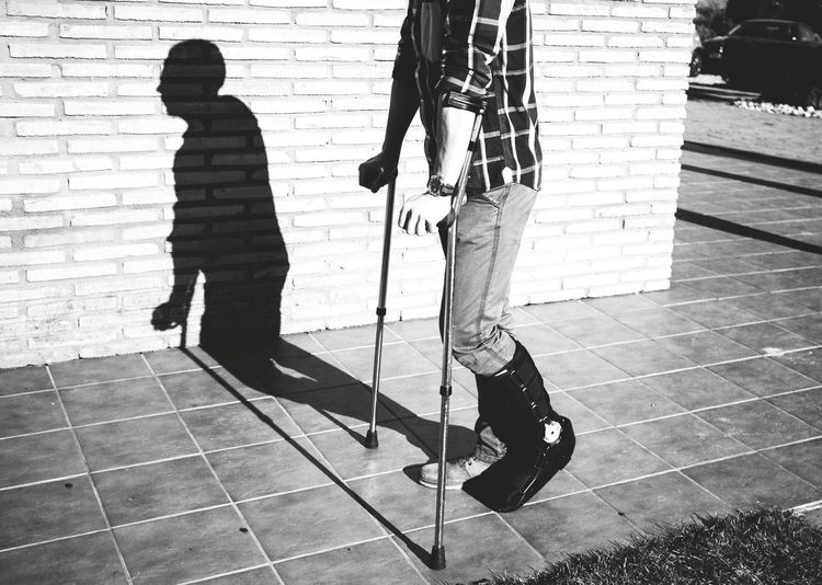 Low section of injured man walking with help of crutches on sidewalk