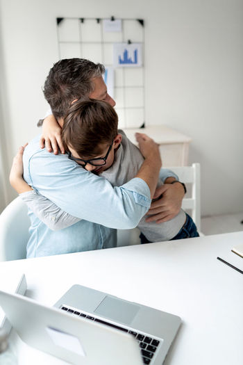 Father and son embracing by laptop on table