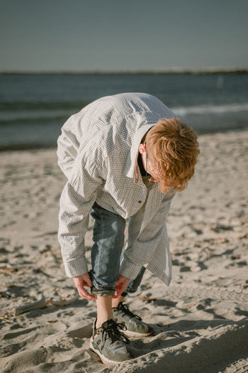 Young man folding jeans standing on beach