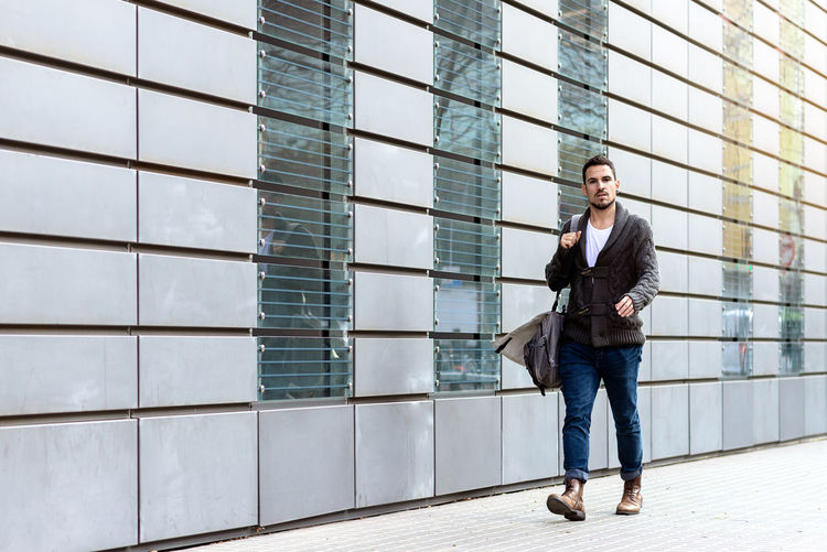 Young bearded man walking on the street next to office building
