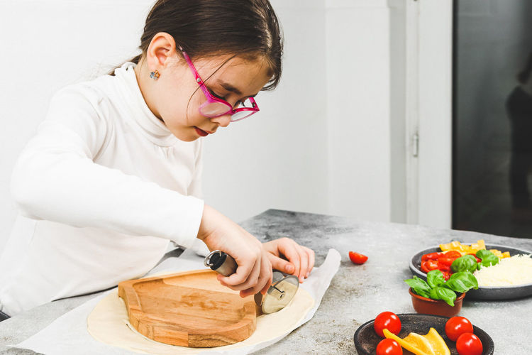 Caucasian girl in a white turtleneck cuts dough on a wooden plate with a metal scabbard.