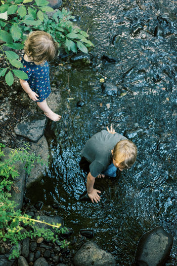 A five year old boy and his little sister looking for rocks in a river