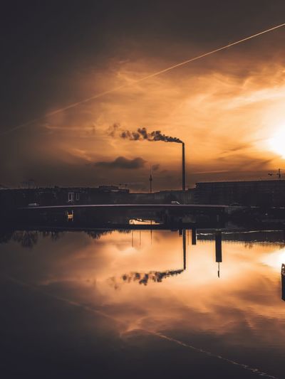 Reflection of factory on lake against sky during sunset