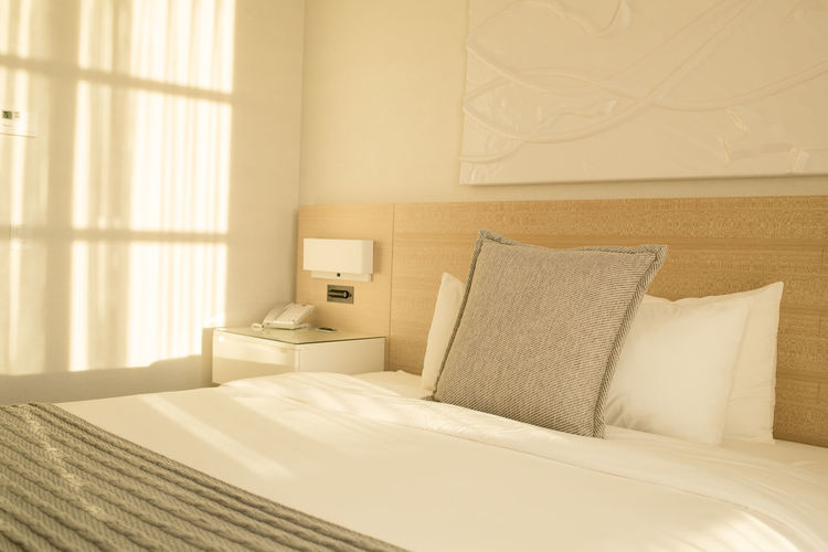 A comfortable hotel room bed with the reflection of the window streaming across it