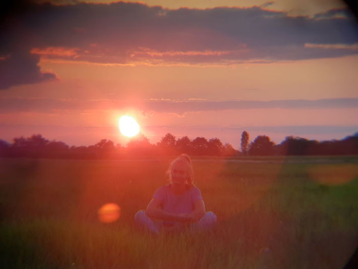 Woman sitting on field against sky during sunset